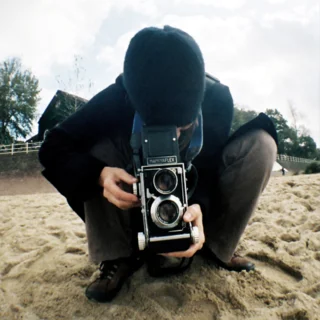 Fotografin mit analogem Fotoapparat kniend in Frontalansicht
